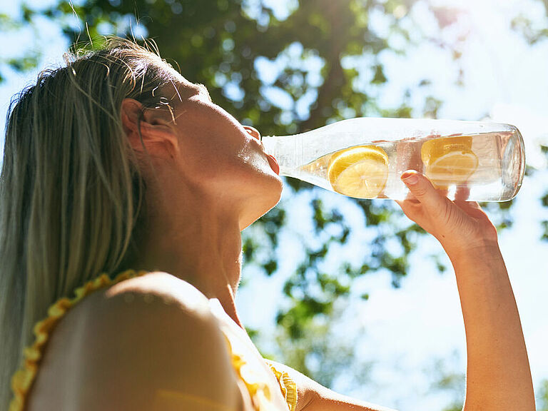 Eine Frau Trinkt bei Hitze aus einer Wasserflasche mit Zitronenscheiben