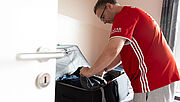 Steven trägt ein rotes Trikot und packt den Koffer, der vor ihm auf dem Bett steht. 