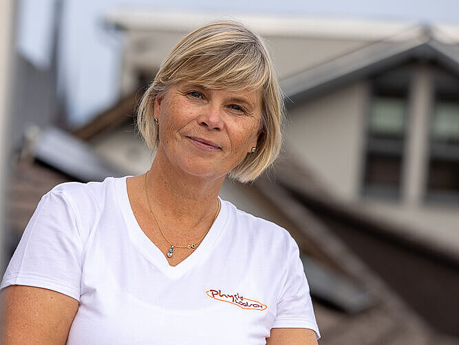 Christine Blass, ist Inhaberin der Praxis „Physiologisch“ in Gau-Algesheim. Sie stützt sich auf einen Mauervorsprung und lacht in die Kamera. 
