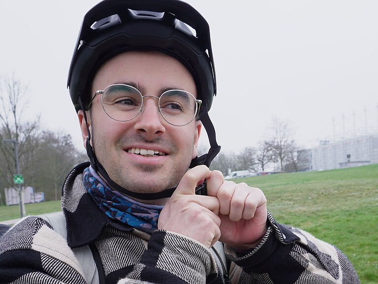  Porträt eines jungen Mannes, der den Verschluss seines Fahrradhelms schließt und freundlich in die Kamera schaut. 