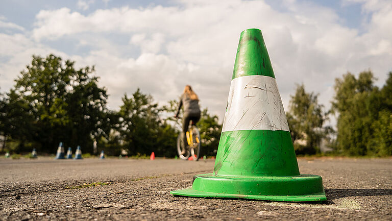 Ein grünes kleines Hütchen im Vordergrund, eine Frau fährt im Hintergrund Rad