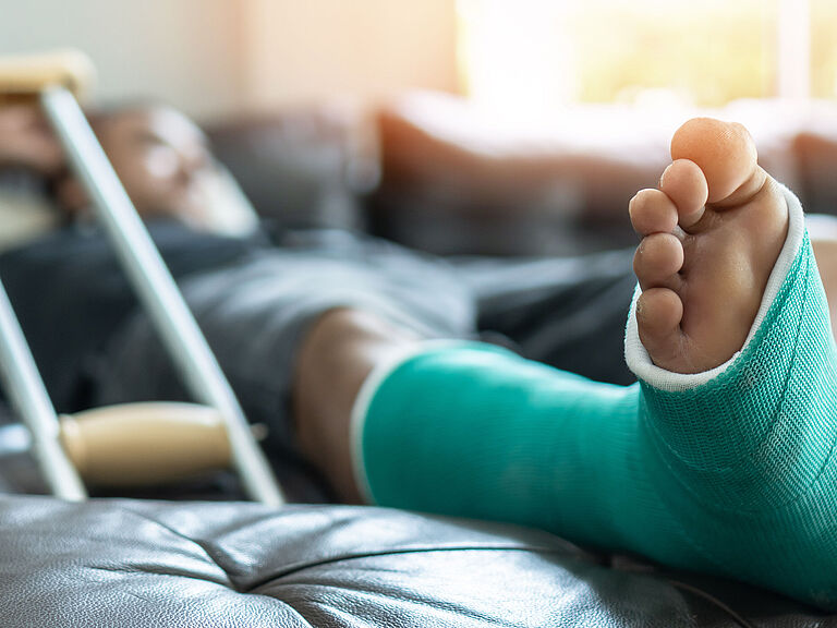 Knochenbruch an Fuß und Bein bei einem männlichen Patienten mit Gipsschiene und Krücken während der chirurgischen Rehabilitation und orthopädischen Genesung zu Hause