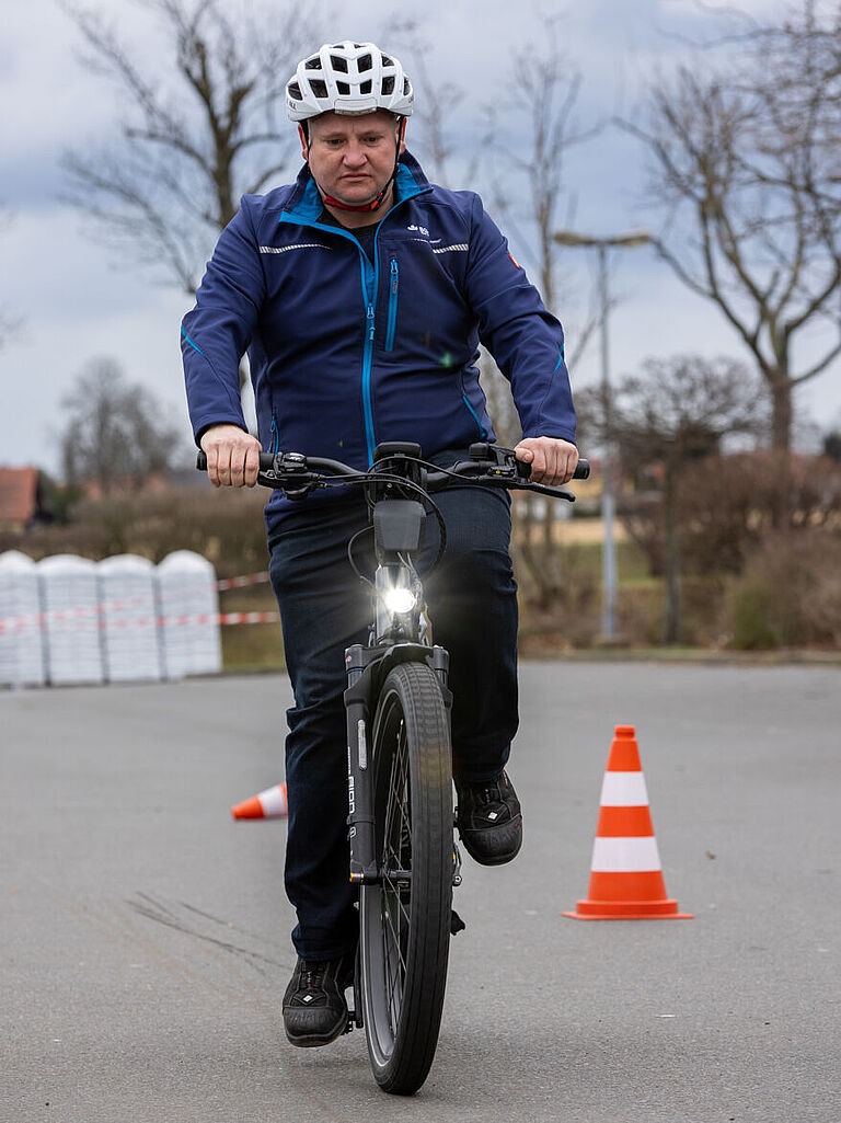 BGHW-Trainer Sven Krämer fährt mit dem E-Bike auf die Kamera zu. Er trägt einen Fahrradhelm. Er zeigt, was beim E-Bike-Fahren zu beachten ist. 