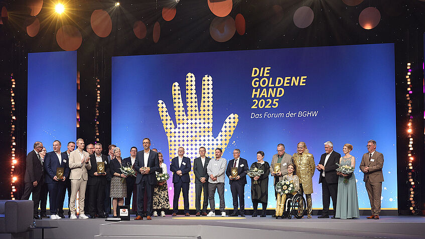 Preisverleihung DIE GOLDENE HAND 2025 in Mannheim. Die Preisträger stehen gemeinsam auf der Bühne. Die Moderatoren im Vordergrund.
