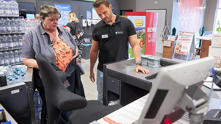 Ergonomie-Trainer berät Supermarktangestellte an der Kasse