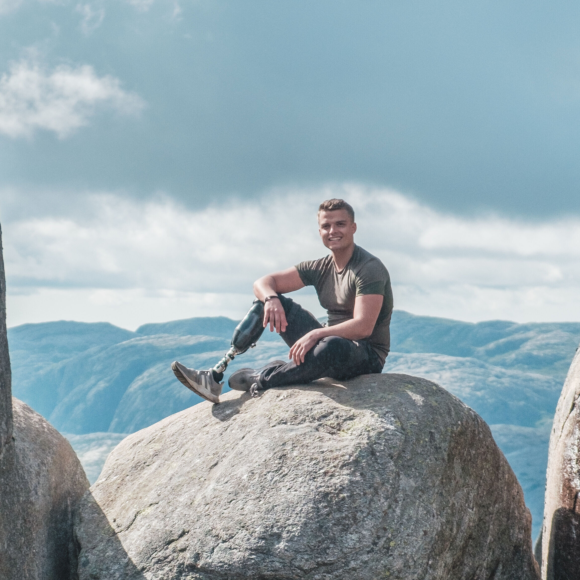 Thomas Müller, ein BGHW-Versicherter aus Köln, dessen rechter Unterschenkel nach einem Unfall amputiert werden musste, sitzt auf einem großen felsigen Stein, der zwischen zwei Felsen on der Luft hängt. n hängt und schaut in die Kamera. Er schaut freundlich in die Kamera.