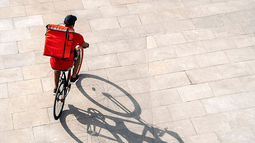 Ein rotgekleideter Fahrradkurier mit rotem Rucksack, von oben fotografiert