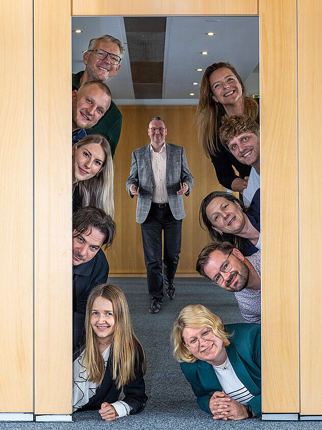 Gruppenbild mit Herrn Schäffner Gruppenbild. Links und rechts von einer geöffneten Tür befinden sich jeweils 5 Personen. Dazwischen steht der Geschäftsführer. Fotomontage.