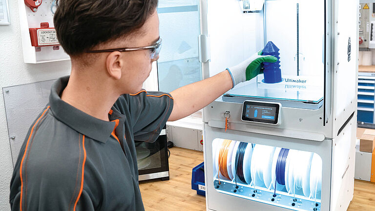 Auszubildender holt aus 3D-Drucker einen hergestellten Bohrschutz