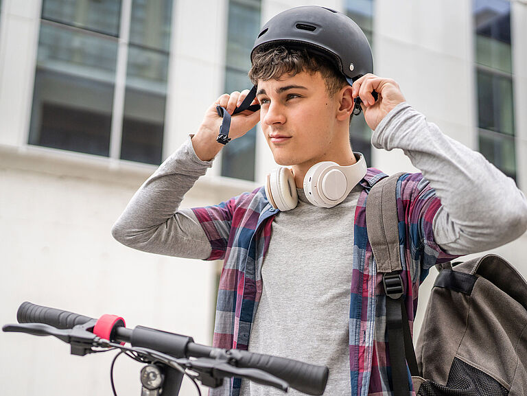 Ein junger Mann sitzt auf dem Fahrrad und schnallt sich gerade seinen Helm um