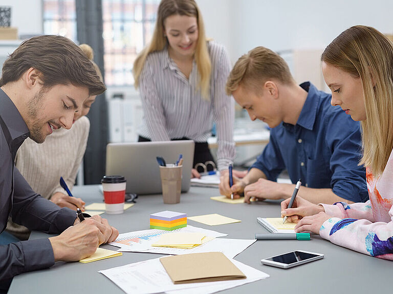 Kleine Seminargruppe von 4 Teilnehmern arbeitet handschriftlich. Dozentin schaut zu.