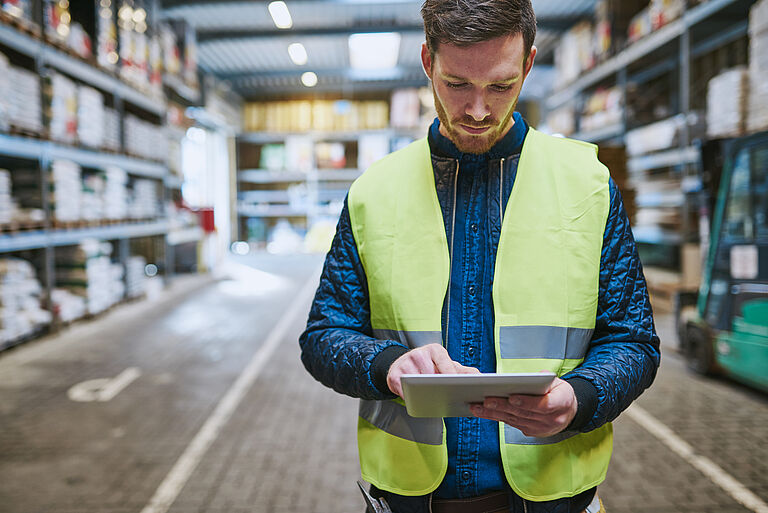 Junger Mann zwischen Lagerregalen bedient ein Tablet