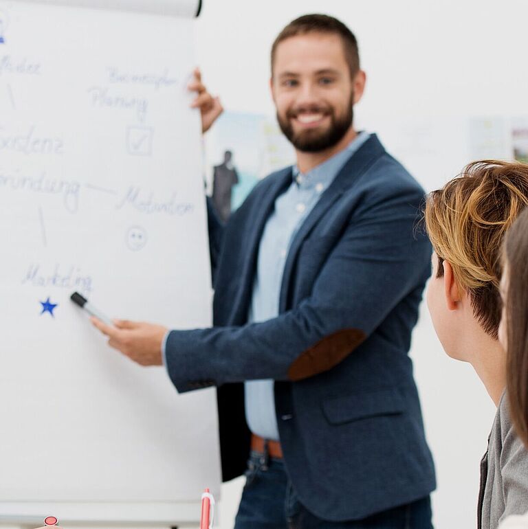 Mann erklärt einer Gruppe von Personen etwas am Flipchart