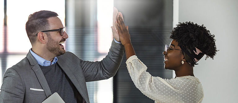 Eine Mitarbeiterin und ein Mitarbeiter in einem Büro geben sich High Five