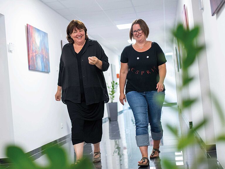 Personalleiterin Claudia Fischer-Curdts und Iris Blümm schlendern lächelnd über den Flur des Verwaltungsgebäudes der Hans Batzner GmBH.