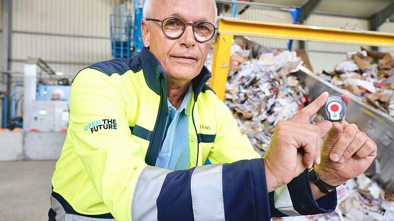 Andreas Sirries, H & S Manager bei Smurfit Kappa Recycling und Fachkraft für Arbeitssicherheit, hockt neben dem Förderband und hält eine Transponderuhr in den Händen. 