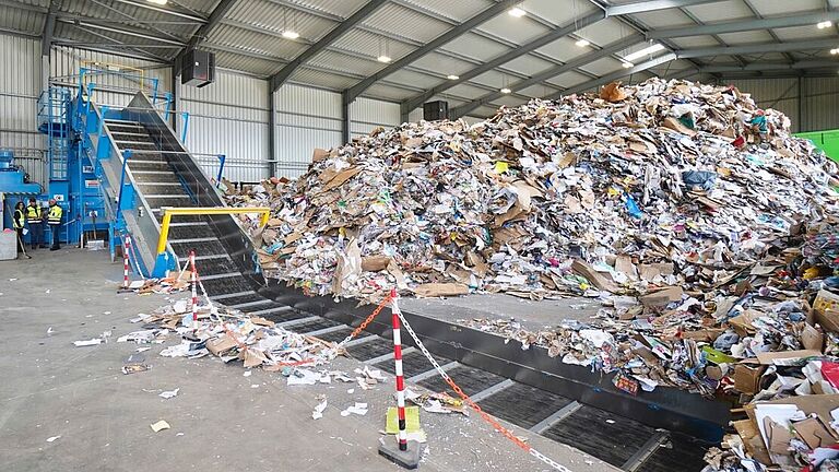 Die Halle von Die Halle von Smurfit Kappa Recycling GmbH mit Kanalballenpresse und Förderband in der Gesamtsicht. Neben dem Förderband türmt sich das lose Altpapier. tonnenweise Altpapier in loser Form zu Ballen presst. 