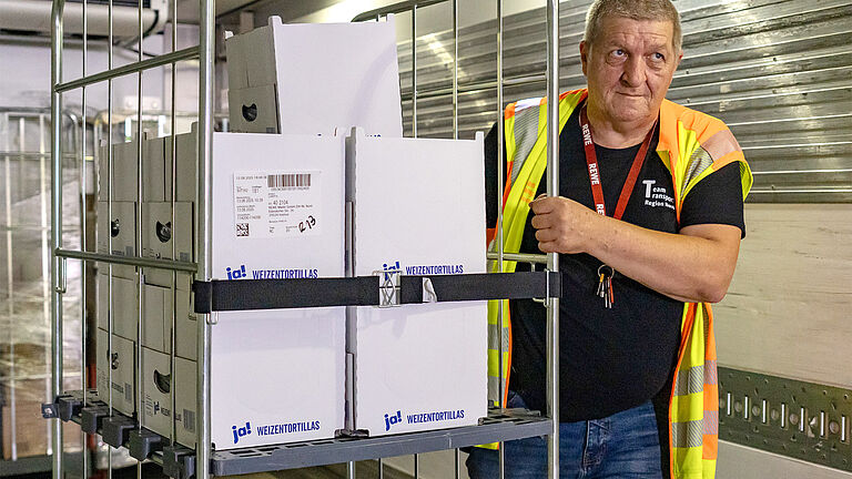 Ein Mann schiebt einen Rollcontainer, der mit dem neuen Gummispanngurt fixiert ist, seitlich neben sich her.