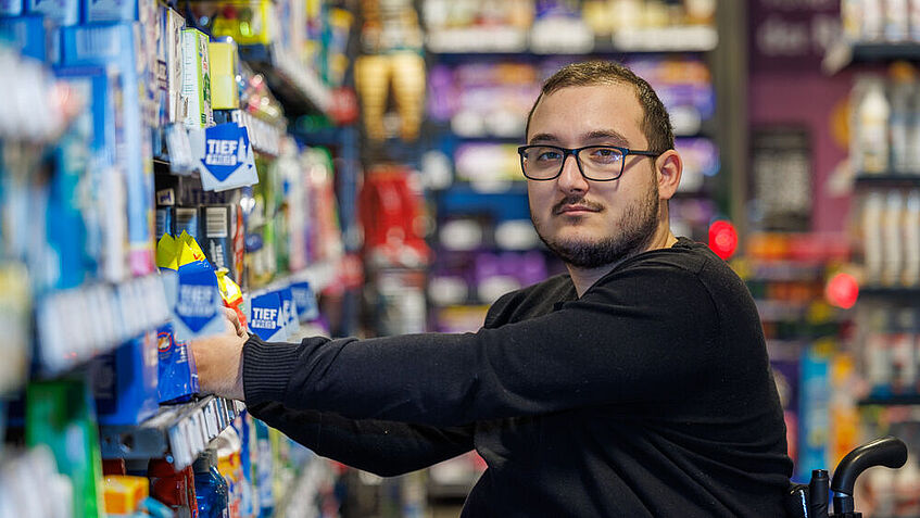 Porträt Rewe-Azubi Achilleas Tsandekidis vor Warenregalen