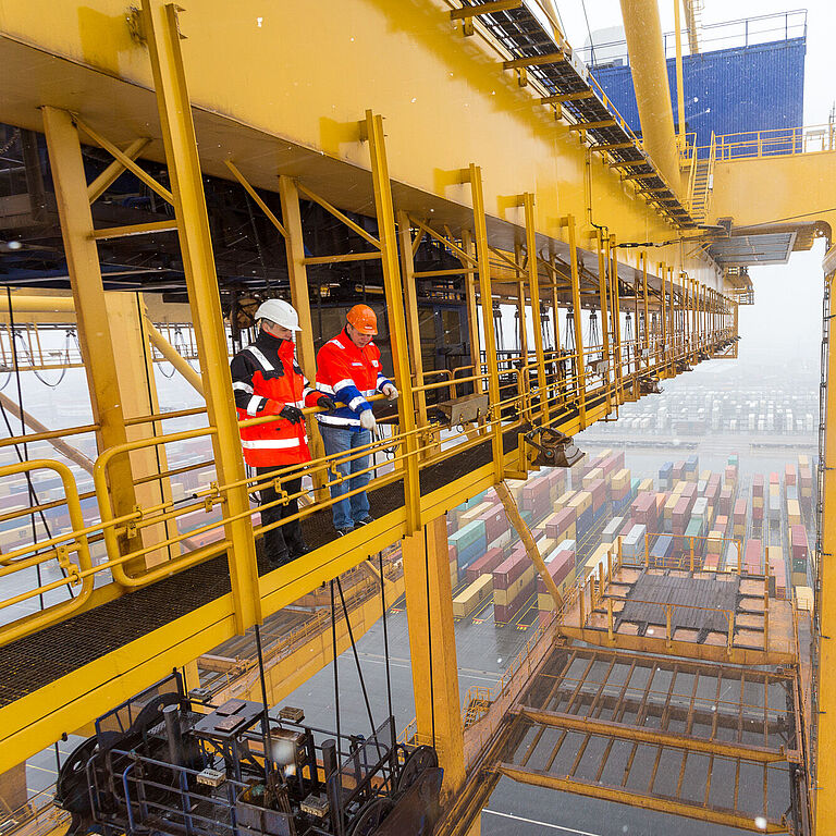 Eine Aufsichtsperson und ein Hafenmitarbeiter überblicken einen Containerhafen aus der Höhe