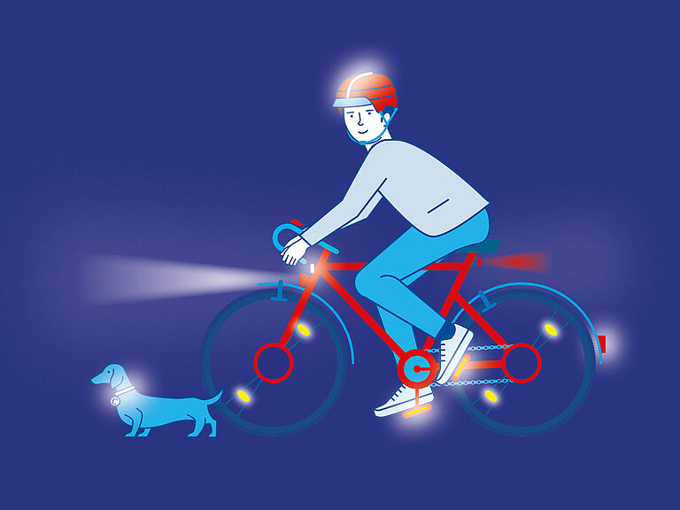 Fahradfahrer, der im Dunkeln mit heller Kleidung sowie Licht und Reflektoren am Fahrrad mit einem Hund unterwegs ist. Sein Helm ist ebenfalls reflektierend wie das Halsband des Hundes.