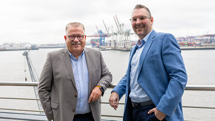 Zwei Männer stehen an einer Reling. Im Hintergrund befindet sich der Hamburger Hafen. Zwei Männer stehen an einer Reling. Im Hintergrund befindet sich der Hamburger Hafen.