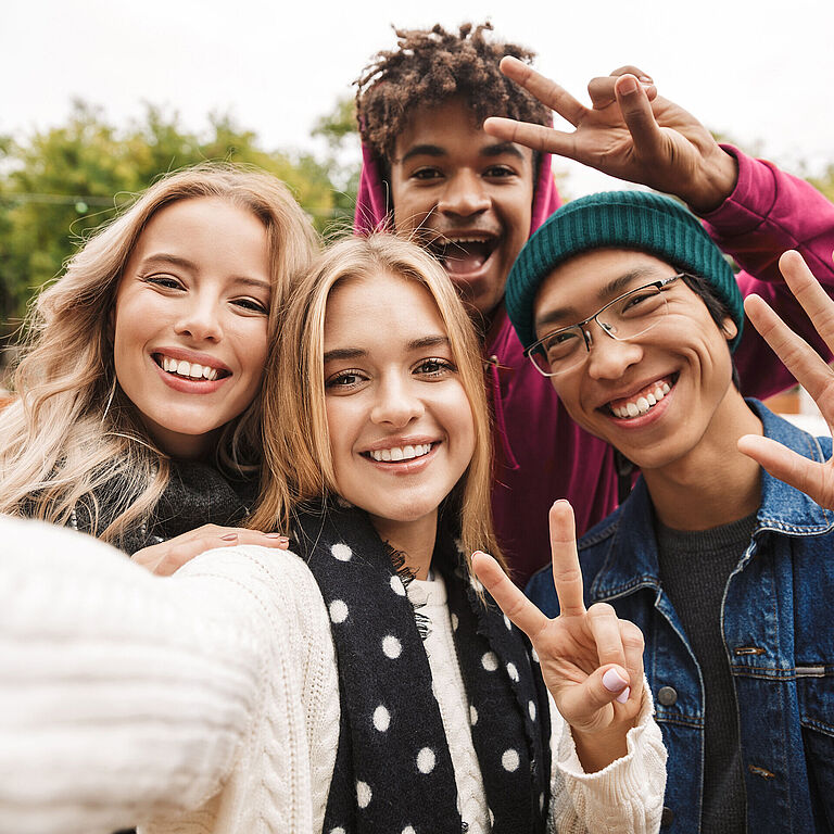 Vier Jugendliche nehmen ein Selfie auf und zeigen das Peace-Zeichen mit ihren Händen