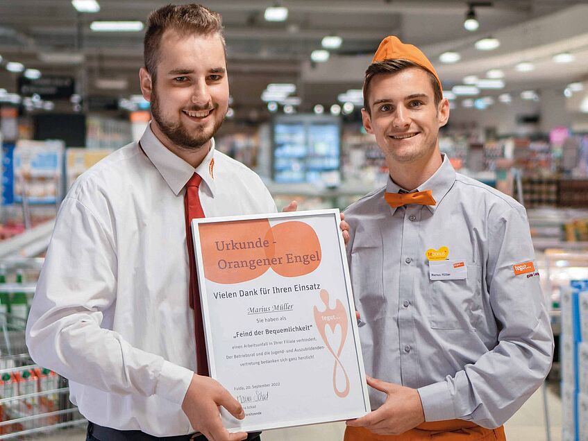 Der Filialleiter überreicht dem Mitarbeiter, der einen Kollegen auf einen Beinahunfall aufmerksam gemacht, die Urkunde Orangener Engel.