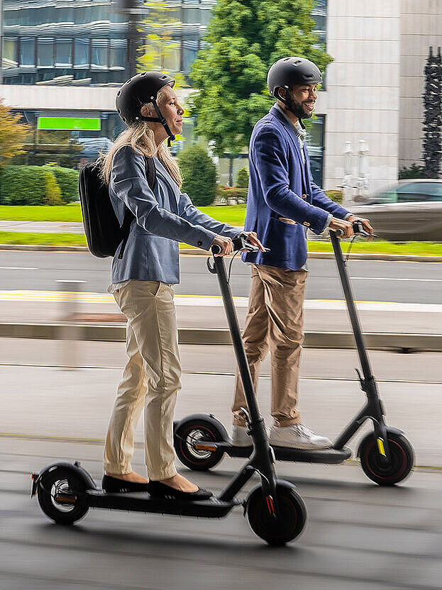 Eine Frau und ein Mann fahren jeweils einen E-Scooter parallel zueinander. 