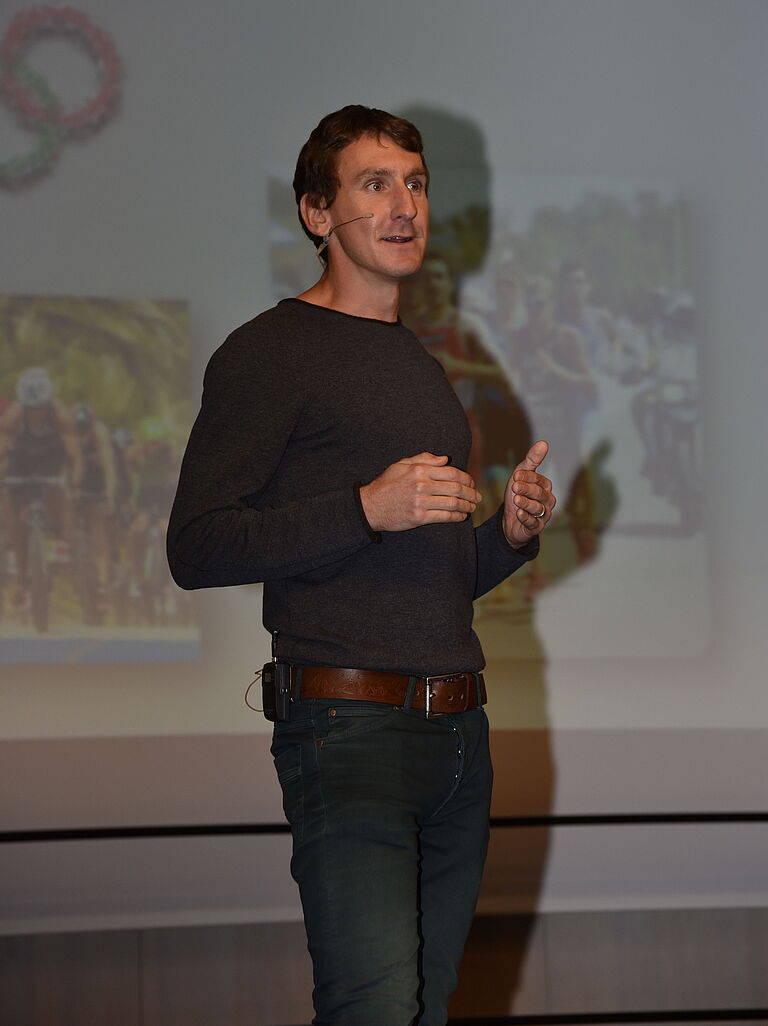 Thomas Springer hält in schwarzem Pullover einen Vortrag vor eine Beamer-Leinwand