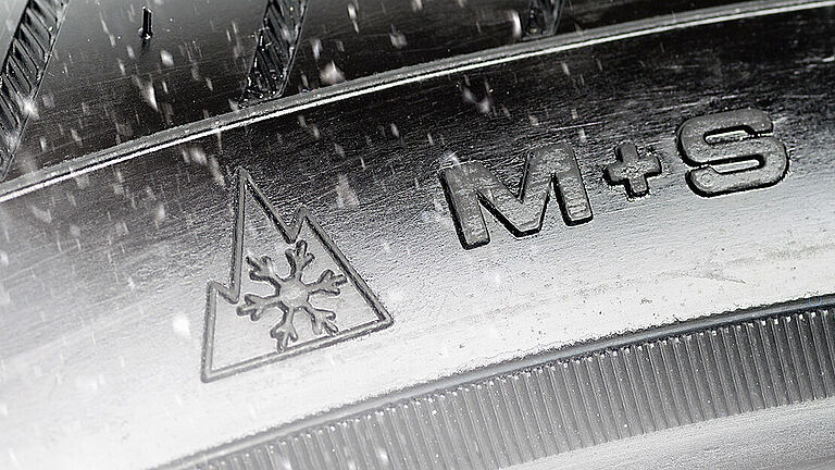 Ausschnitt eines Winterreifen, der das Alpine-Symbol trägt, eine Schneeflocke vor einem Berggipfel