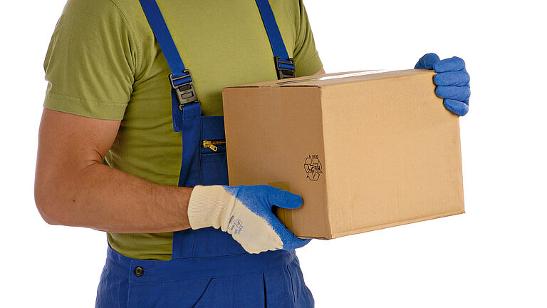 Ein Arbeiter in Latzhose trägt ein größeres Paket