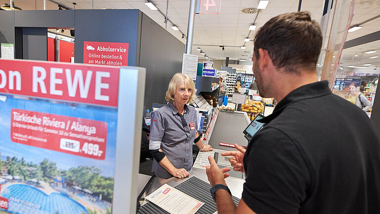 Ergonomie-Trainer berät Supermarktangestellte an der Kasse