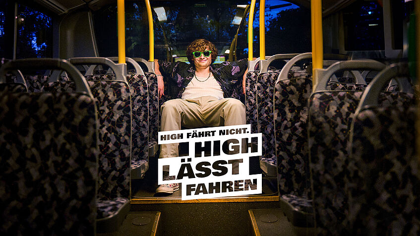 Ein junger Mann mit lockigen Haaren, Sonnenbrille und lässiger Kleidung sitzt entspannt auf der Rückbank eines leeren Busses. Auf dem Bild steht der Slogan: „High fährt nicht. High lässt fahren.“