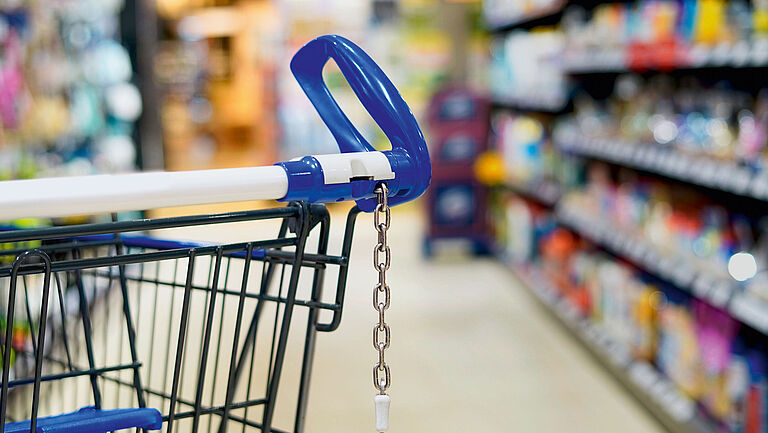 Auf dem Bild ist ein Einkaufswagen in einem Regalgang im Supermarkt zu sehen.