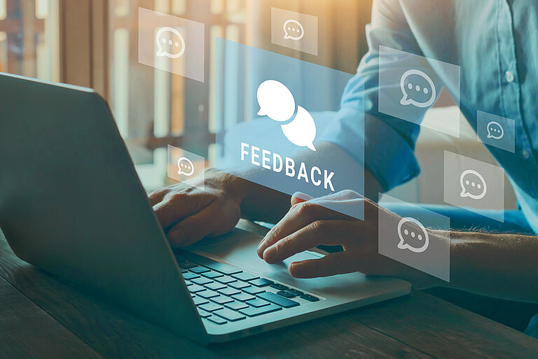Person tippt auf Laptop, Feedback-Symbole schweben dazwischen.