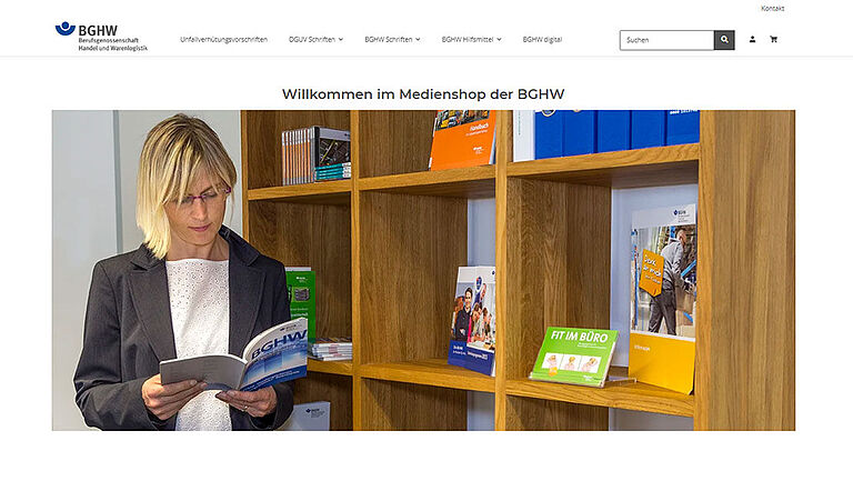 Eine blonde Frau steht vor einem mit Büchern und Printmedien bestückten Regal. Sie schaut in ein Buch.