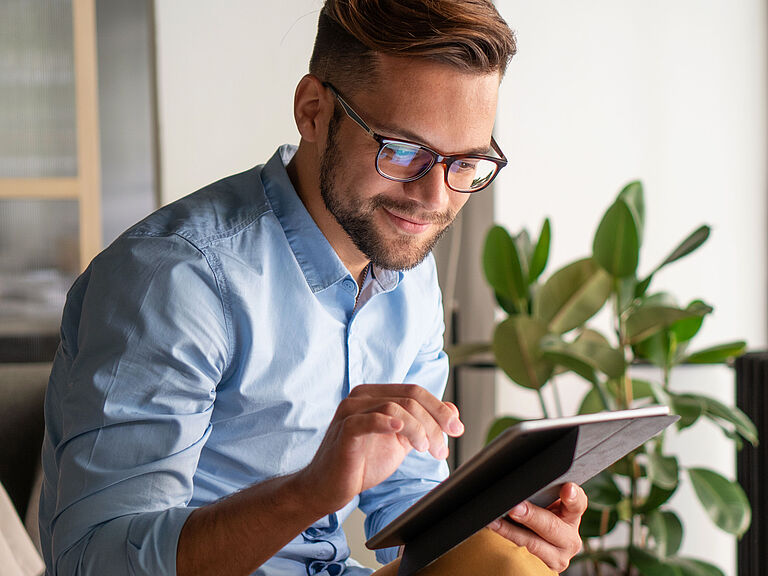 Ein junger, lächelnder Mann, der auf einem Tablet tippt