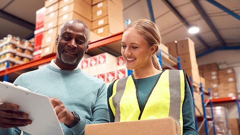 Ein Mitarbeiter und eine Auszubildende im Lager blicken gemeinsam auf ein Dokument
