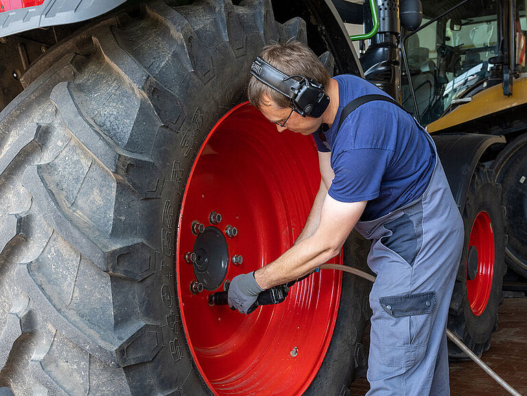 Ein Monteur arbeitet mit einem Schlagschrauber am Reifen eines Traktors