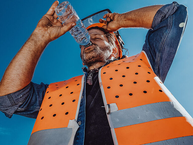 Arbeiter mit Warnweste trinkt bei Hitze an einer Flasche Wasser