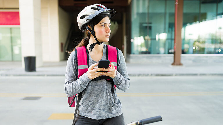 Eine junge Frau sitzt auf dem Fahrrad und hält ihr Smartphone in der Hand