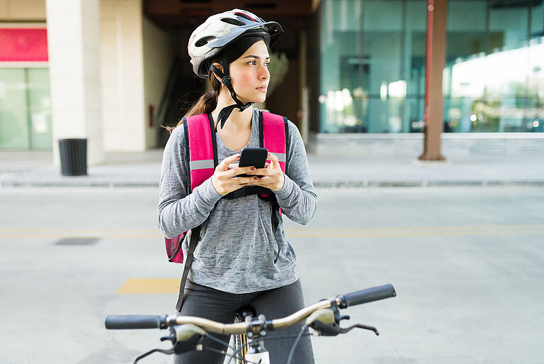 Eine junge Frau sitzt auf dem Fahrrad und hält ihr Smartphone in der Hand
