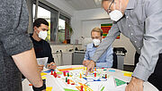 Vier Personen stehen um einen Tisch, darauf liegt das Managementtool, das wie ein Spielfeld aussieht.