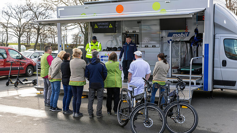 Mehrere Personen stehen mit dem Rücken zur Kamera. Sie hören den Trainern des BGHW-mobil zu, die zum Thema Sicherheit informieren. 