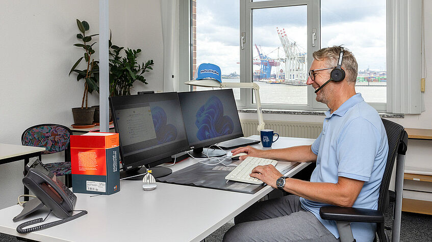 Ein Mann sitzt in seinem Büro am Schreibtisch vor einem PC. Er hat ein Headset an. Ein Mann sitzt in seinem Büro am Schreibtisch vor einem PC. Er hat ein Headset an.