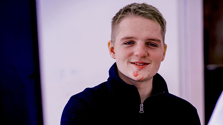 Porträtfoto von Lars Eberhard. Er trägt einen dunklen Pulli und schaut freundlich in die Kamera. Seine verletzte rechte Hand ist unscharf im Vordergrund zu sehen. 