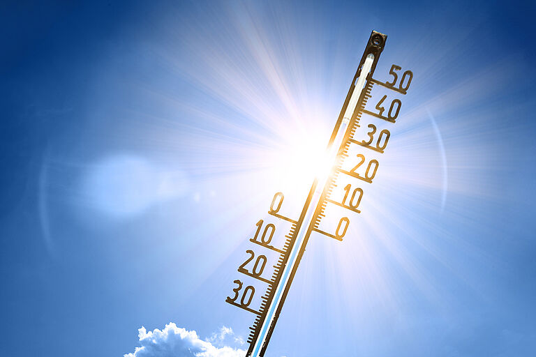 Ein Thermometer ragt in den sonnigen Himmel. Es zeigt 34 Grad Celsius an.