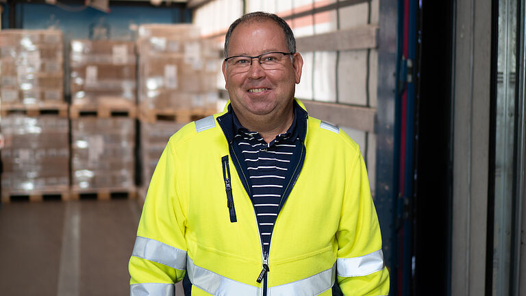 Porträt Fachkraft für Arbeitssicherheit Andreas Neumaier in gelber Warnschutzjacke im Logistikzentrum.