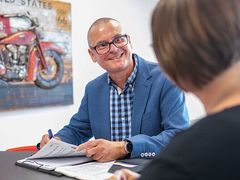 BGWH Reha-Berater Armin Lohr steht mit der Patientin und ihrer Akte am Besprechungstisch. 